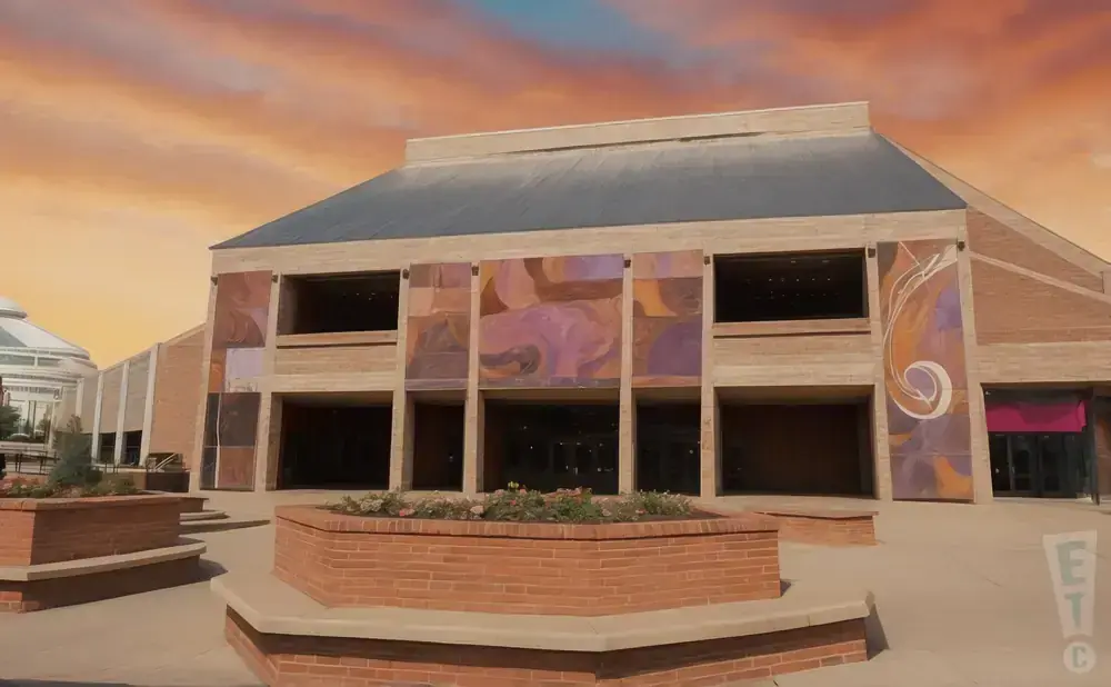 An abstract mural adorns the brick facade of a modern building under a dramatic orange sky.