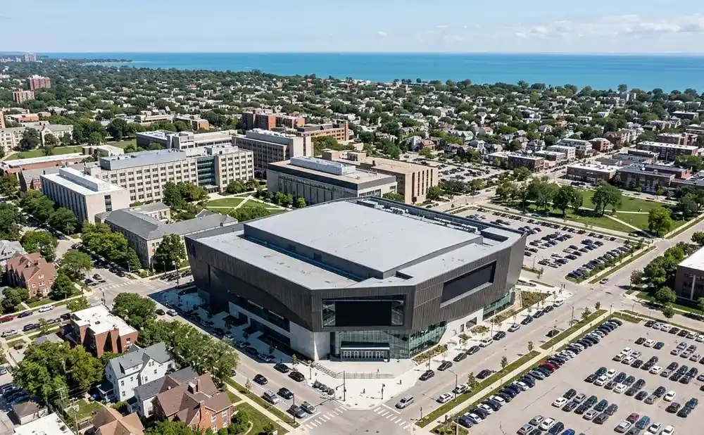Aerial view of a modern university campus with a large building in the foreground and lake in the background.