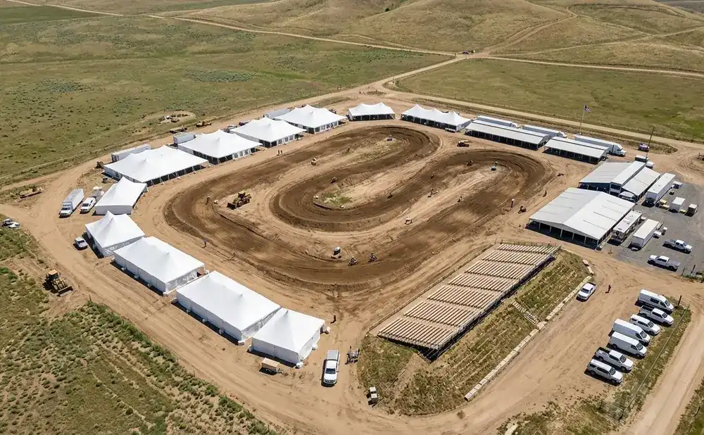 Aerial view of a motocross track with tents, bleachers, and vehicles.