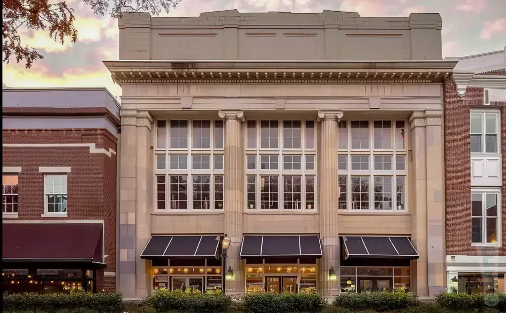 A grand building with large windows and columns, flanked by brick buildings.