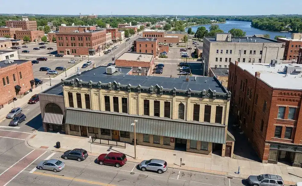 Aerial view of a historic downtown with brick buildings, a river in the background, and cars parked on the street.