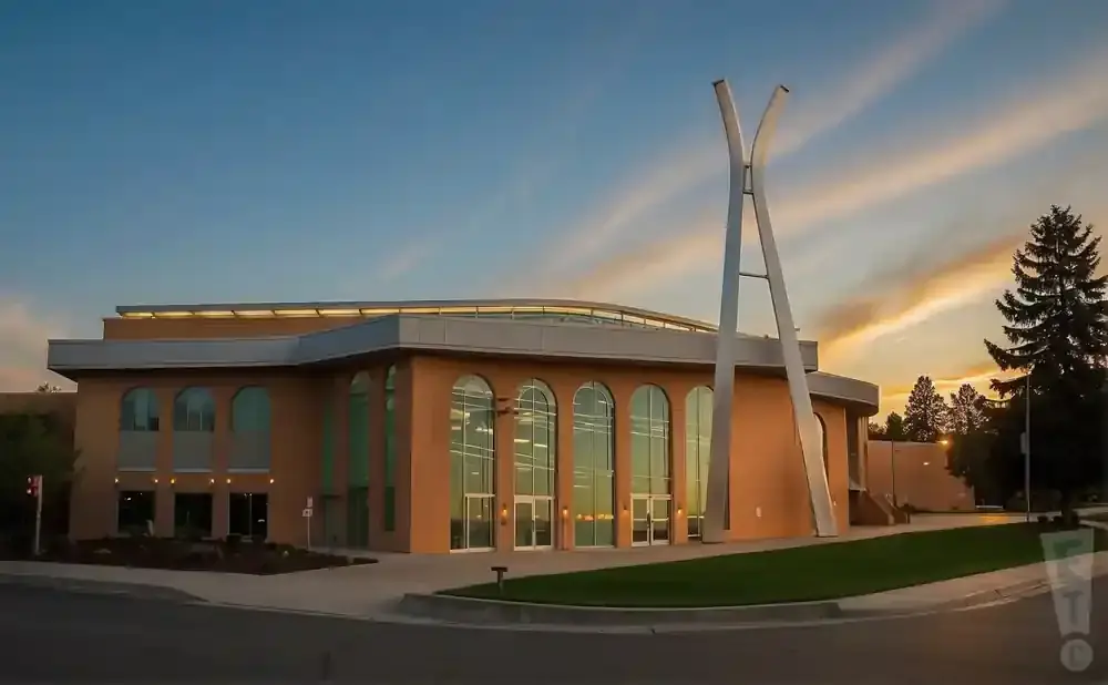 Modern building with arched windows and a tall, abstract sculpture at sunset.