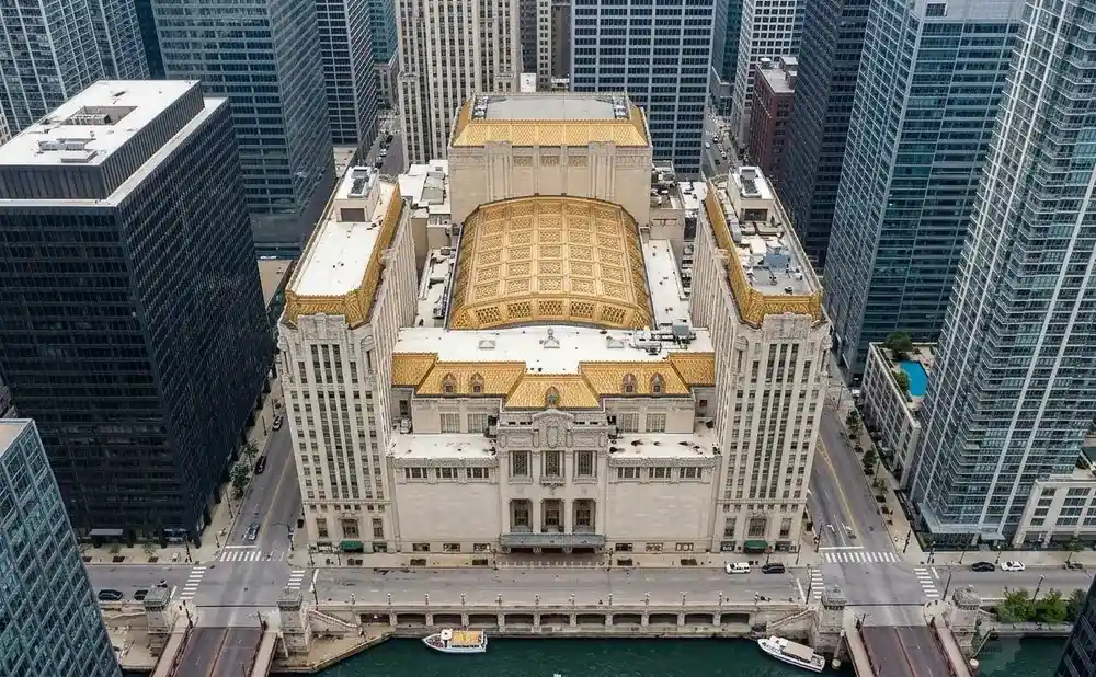 Aerial view of a large, ornate building with a gold roof, surrounded by tall skyscrapers and a river.