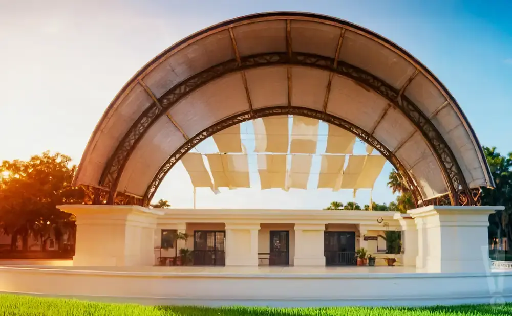 An outdoor stage with a large arched canopy, decorated with fabric panels, under a bright sky.