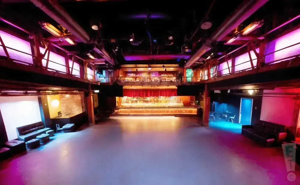 An empty nightclub with a stage, bar, and seating.