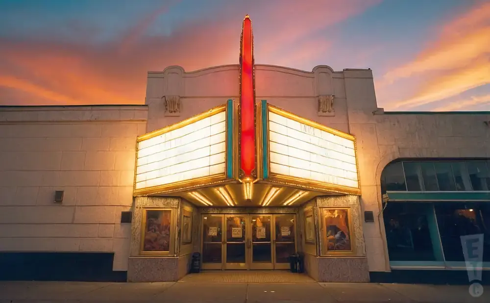 A vintage theater marquee glows against a colorful sunset sky.