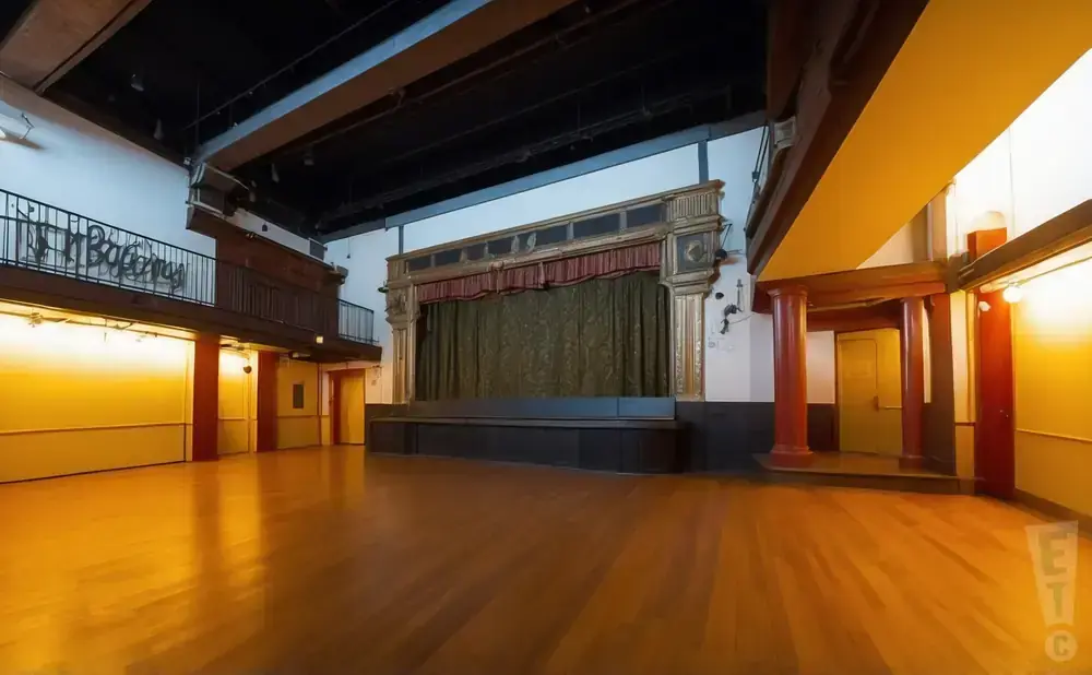Empty theater with stage, dark curtains, and wooden floor.