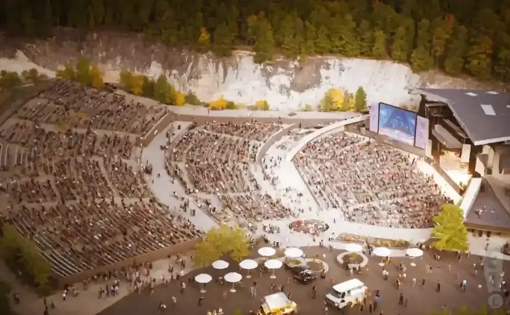 An aerial view of an outdoor amphitheater with a large crowd enjoying a performance on a stage with screens.