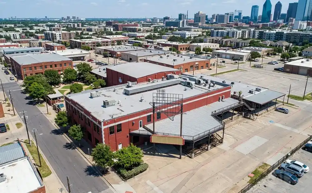 Aerial view of a red brick building with a large Texas-shaped sign and a marquee, surrounded by parking lots and trees.