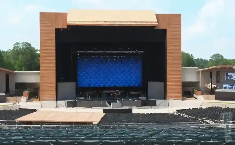 An outdoor amphitheater stage with a large blue screen and empty seats.