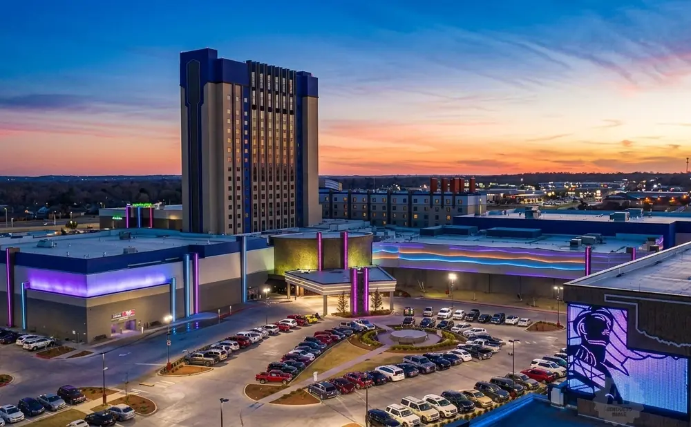 Aerial view of a casino at sunset with a tall hotel tower and illuminated buildings.