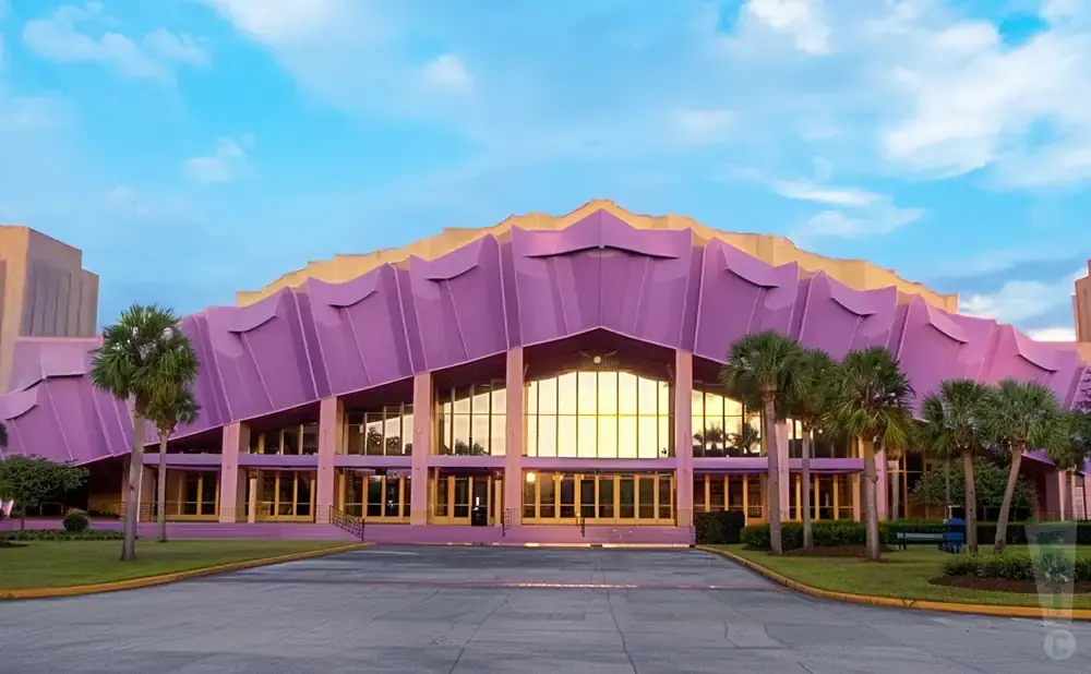 A vibrant purple and gold building with palm trees in front and a blue sky above.