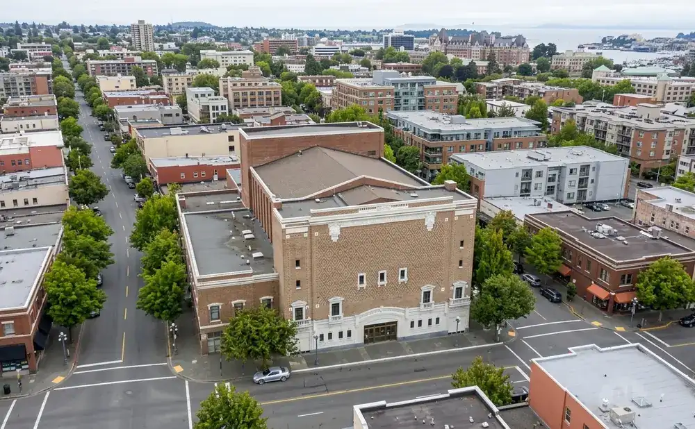 Aerial view of a street lined with brick buildings and trees, leading to a large theater.