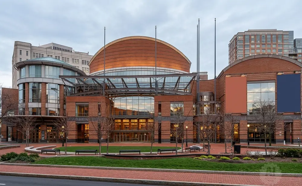 Modern brick theater building with a domed roof, large glass windows, and surrounding trees.