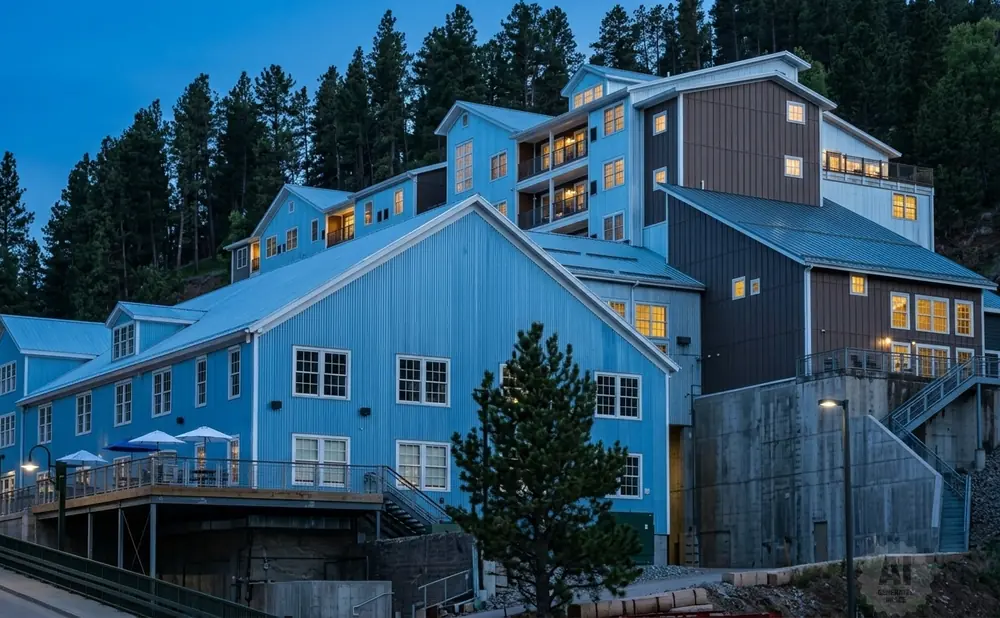 A modern, multi-level blue and brown building nestled into a hillside forest.