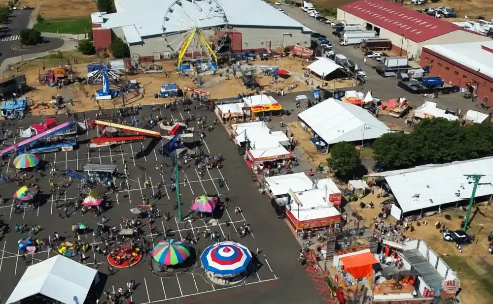 An aerial view of a busy fairground with rides, tents, food stalls, and many people.