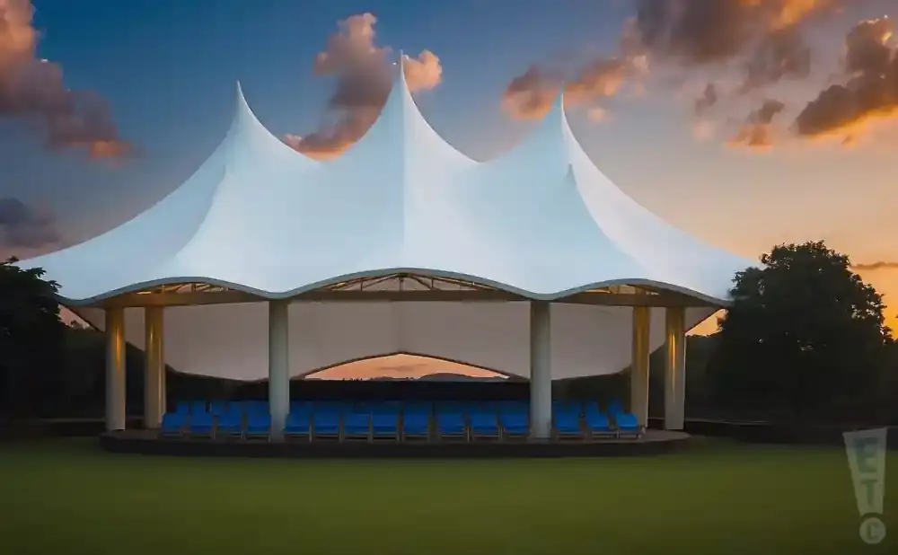 An outdoor amphitheater with a white tent roof and blue seats at sunset.