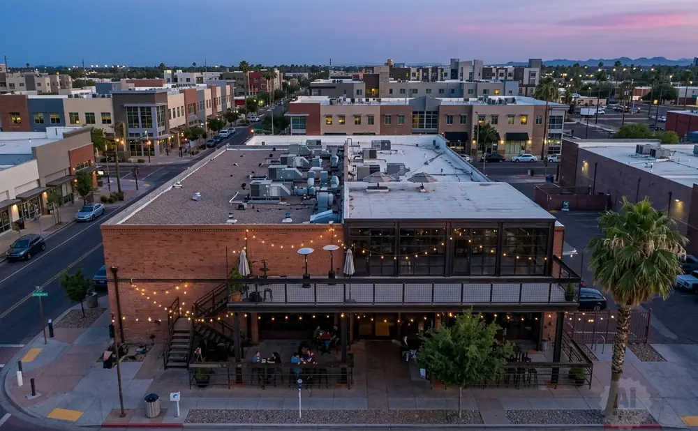 Aerial view of a modern brick building with outdoor seating and string lights at dusk.