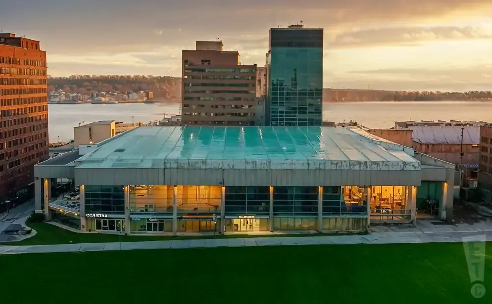 A modern building with a glass roof and facade on a waterfront at sunset.