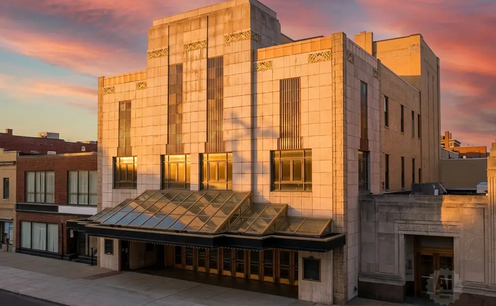 Art Deco theater entrance with glass canopy and ornate facade under a colorful sunset sky.