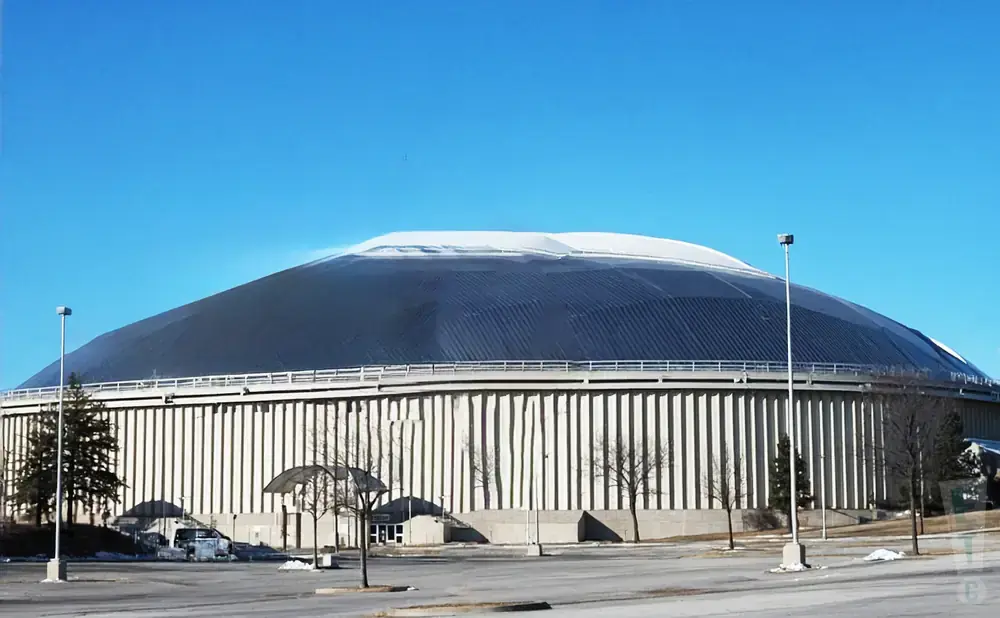 Large domed stadium with a dark roof and a white top, under a clear blue sky.