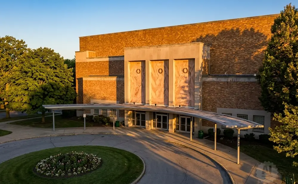 Entrance of a brick building with a covered walkway and a circular flower bed in front.