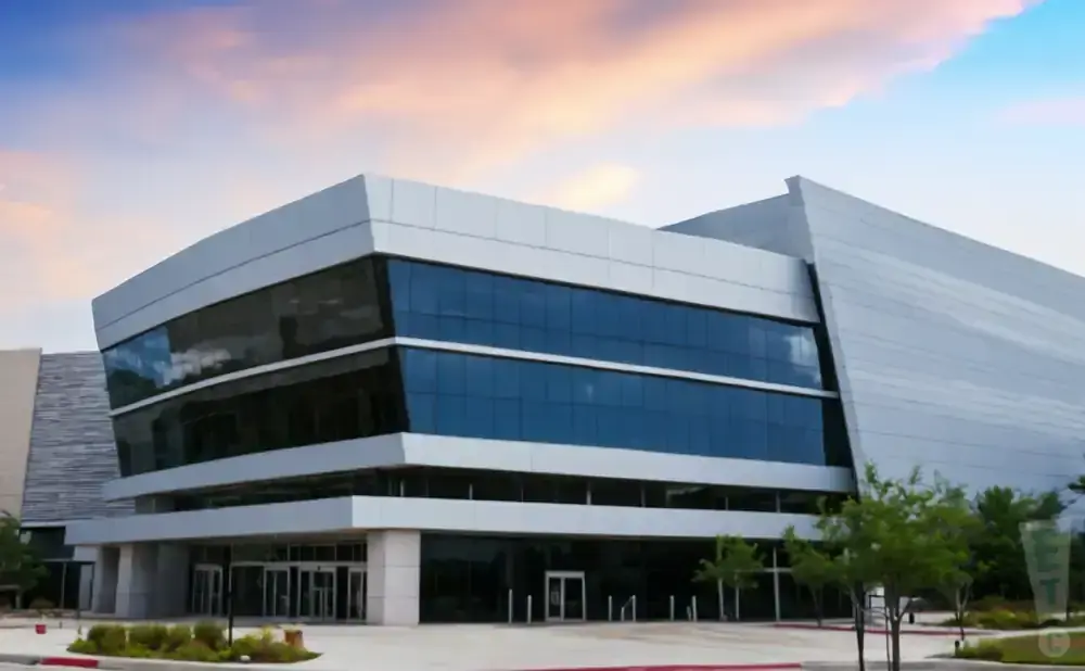 A modern, angular building with dark windows and silver siding against a sunset sky.