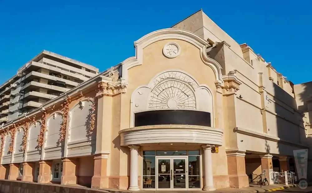 Exterior of a beige building with decorative arches and a sunburst motif, against a bright blue sky.