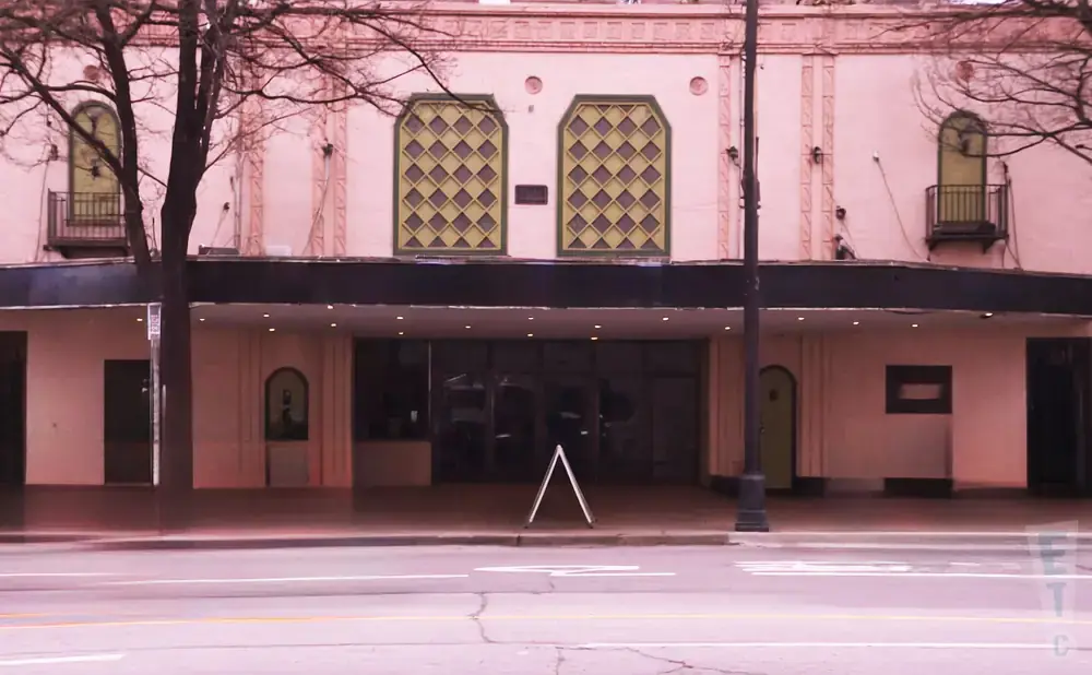 Maroon-pink theater building with arched windows, a marquee, and a sidewalk with an A-frame sign.