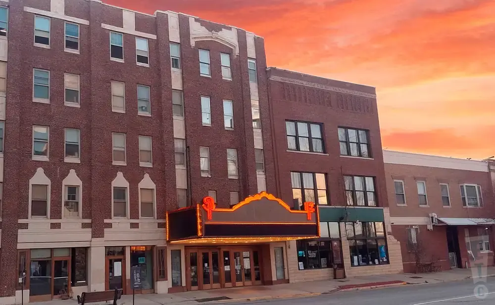 A vintage theater marquee with glowing lights, set against a brick building during a vibrant sunset.