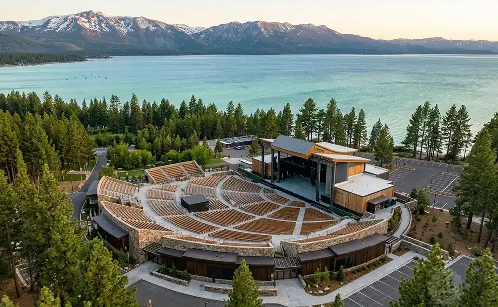 Aerial view of an outdoor amphitheater by a large lake and snow-capped mountains.