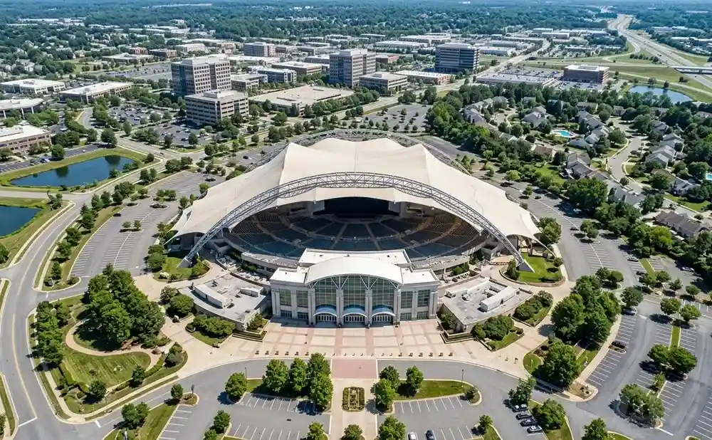 Aerial view of an amphitheater with a large white canopy, surrounded by trees, parking lots, and buildings.