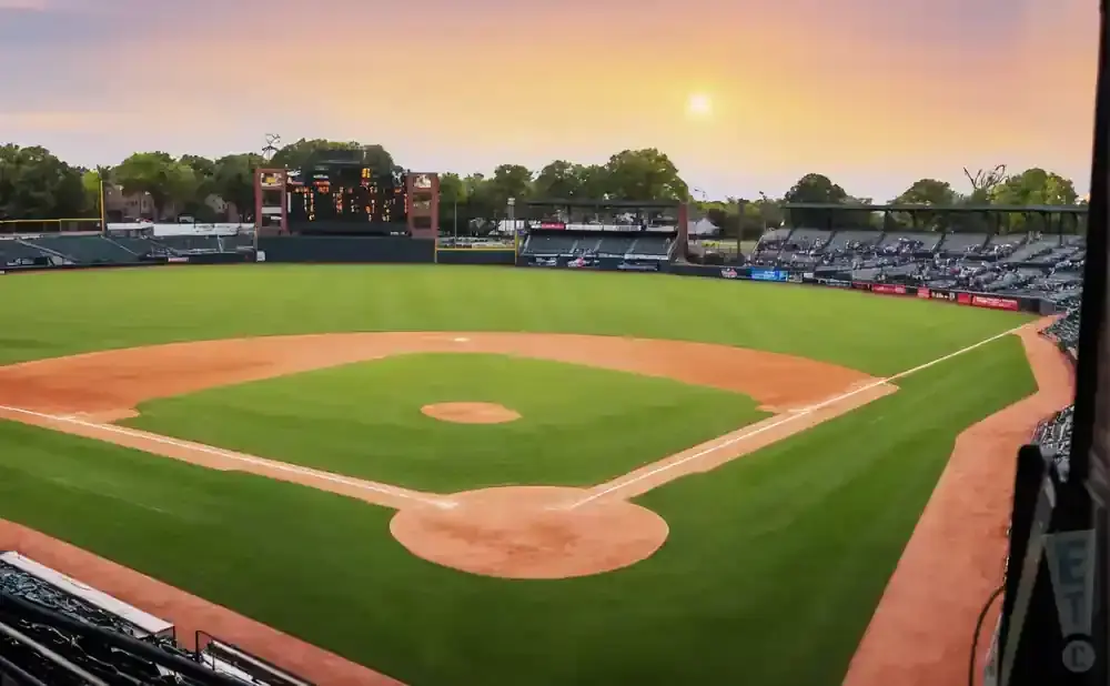 A baseball field at sunset with a scoreboard and empty seats.