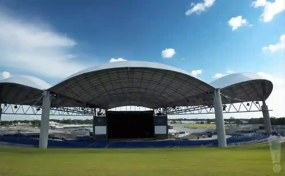 An outdoor amphitheater with a curved white canopy over a stage and seating area.
