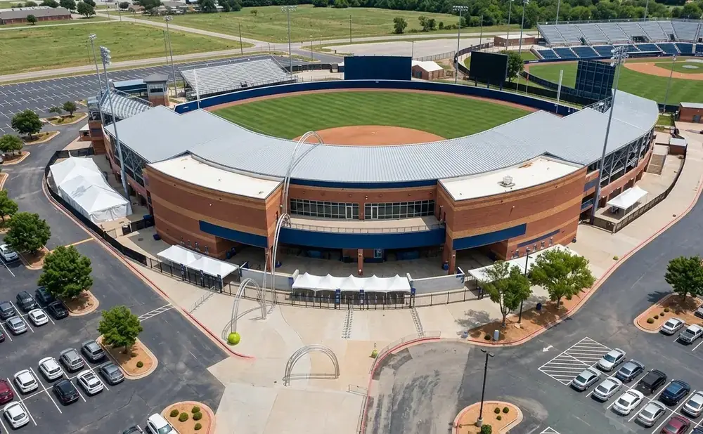 Aerial view of a baseball stadium with a brick building, a baseball field, and surrounding parking lots.
