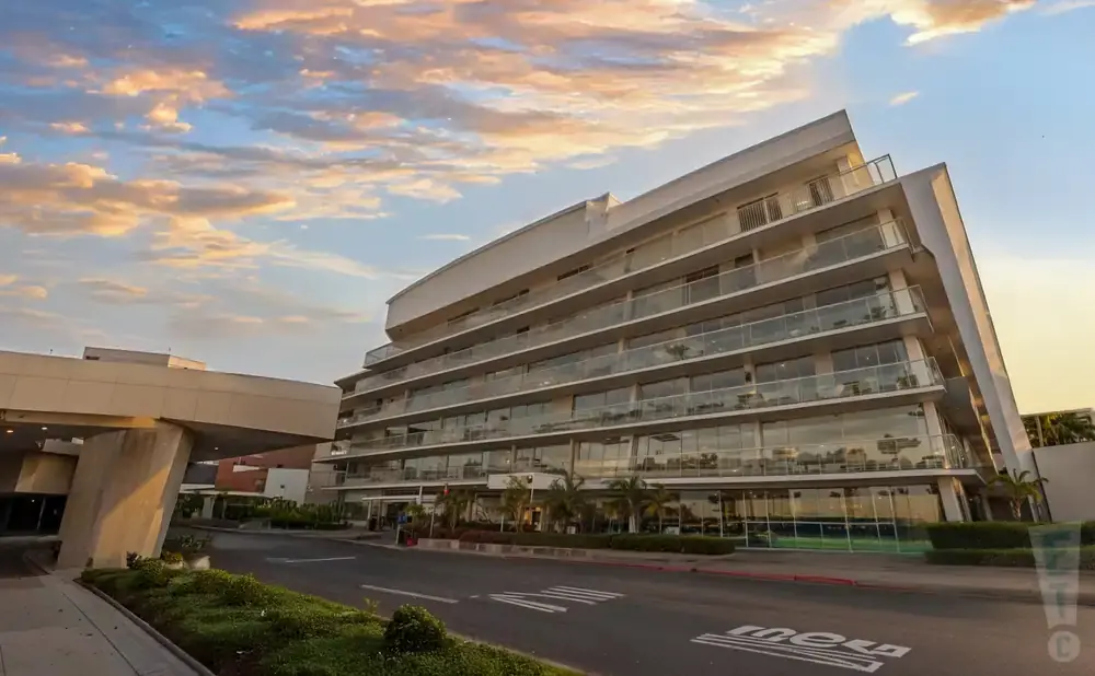 Modern multi-story building with glass balconies at sunset, with a large concrete structure on the left.