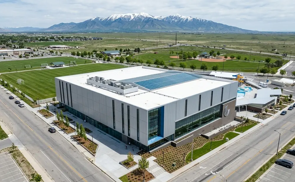 Aerial view of a modern sports complex with soccer fields, a swimming pool, and mountains in the background.