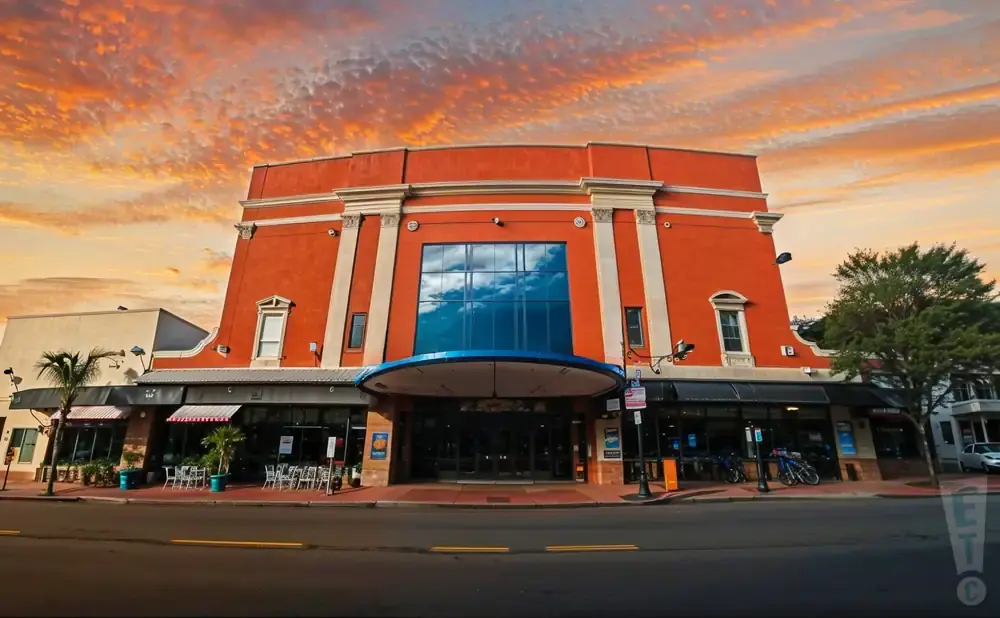 Wide shot of an orange building with a large glass window, under a dramatic sunset sky.