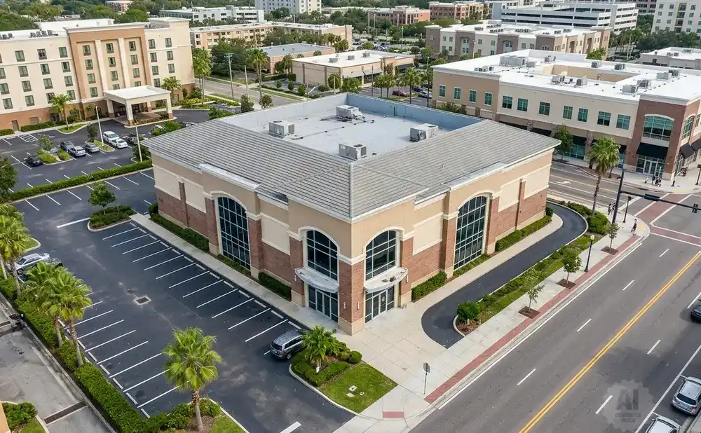 Aerial view of a modern building with a large parking lot, surrounded by other buildings and a street.