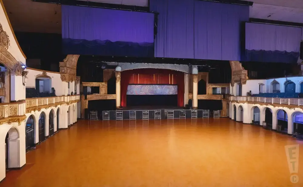 An empty grand ballroom with a stage and balcony seating.