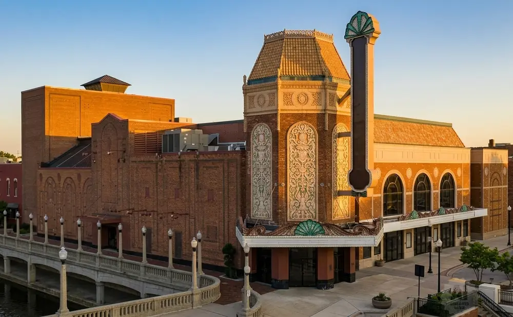 Historic brick theater with ornate details and marquee, adjacent to a stone bridge over a canal.
