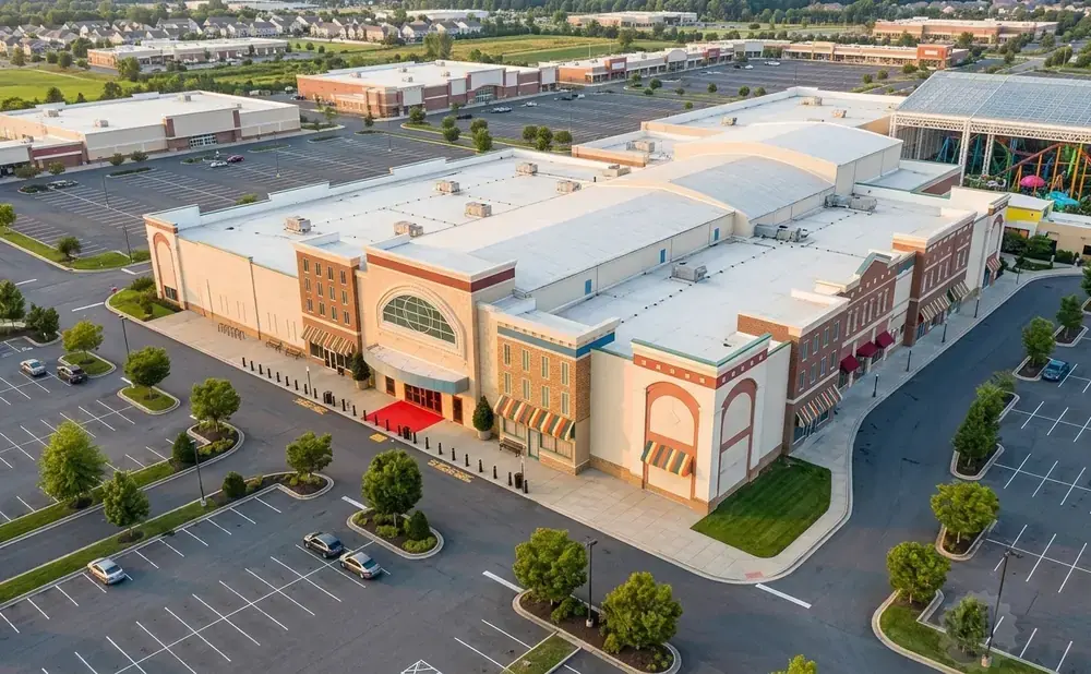 Aerial view of a large shopping mall with a glass-enclosed entertainment area, parking lots, and surrounding buildings.