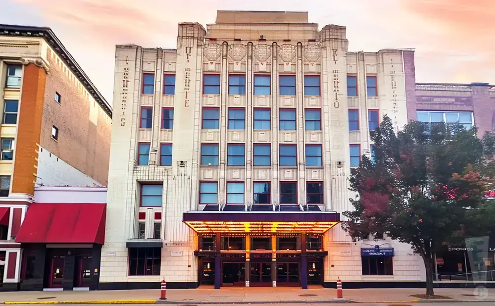 Art deco theater with a lit marquee and blue windows, under a pastel sky.