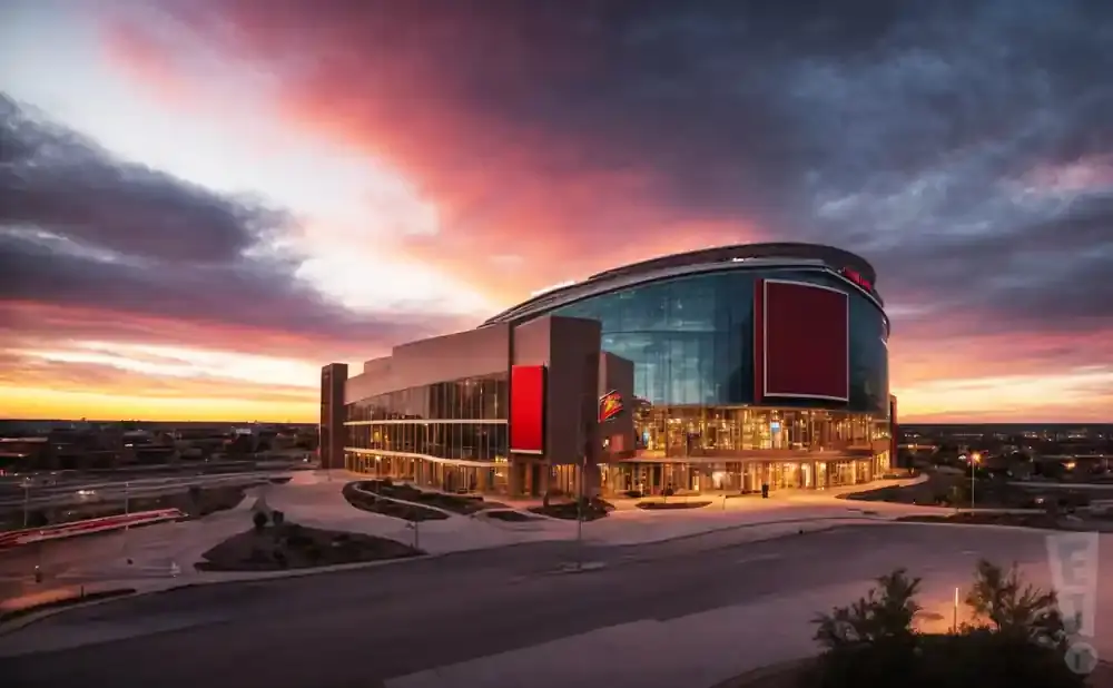 A modern stadium with a glass facade at sunset with a vibrant orange and purple sky.