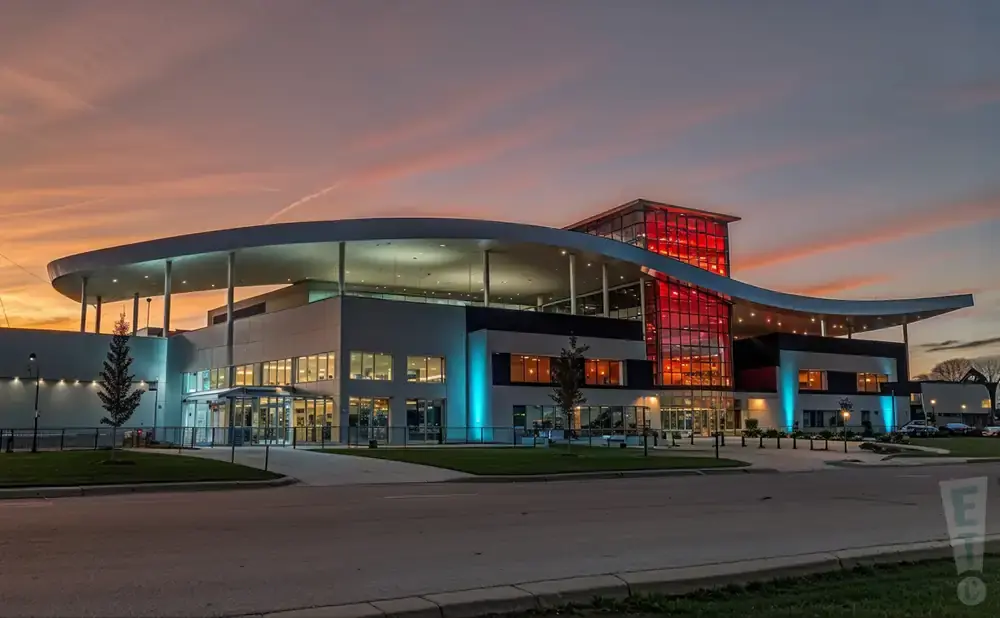 Modern building with a curved roof and red glass tower at sunset.