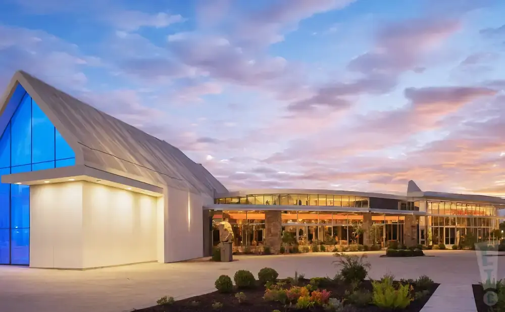 Modern building with a large blue triangular window, lit up at dusk under a colorful sky.