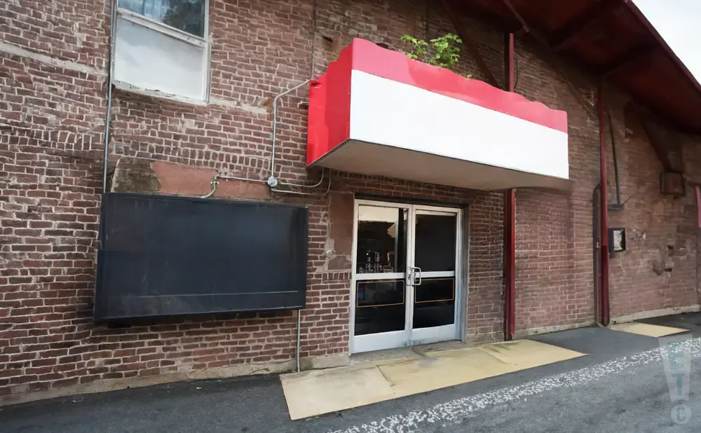 A brick building with double glass doors, a red and white awning, and a large black sign.