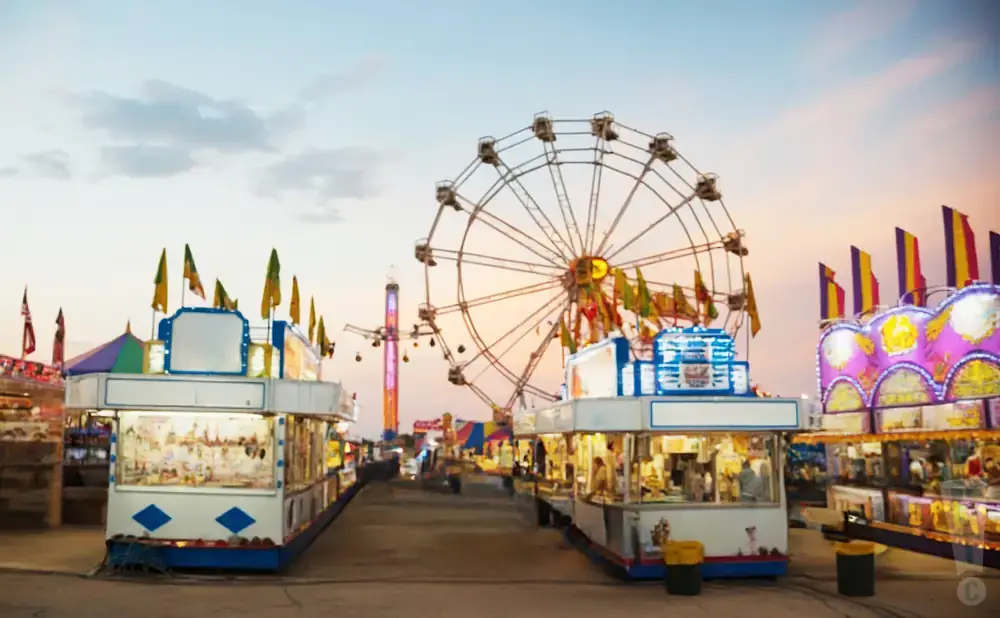 Amusement park at sunset with Ferris wheel, rides, and game booths.