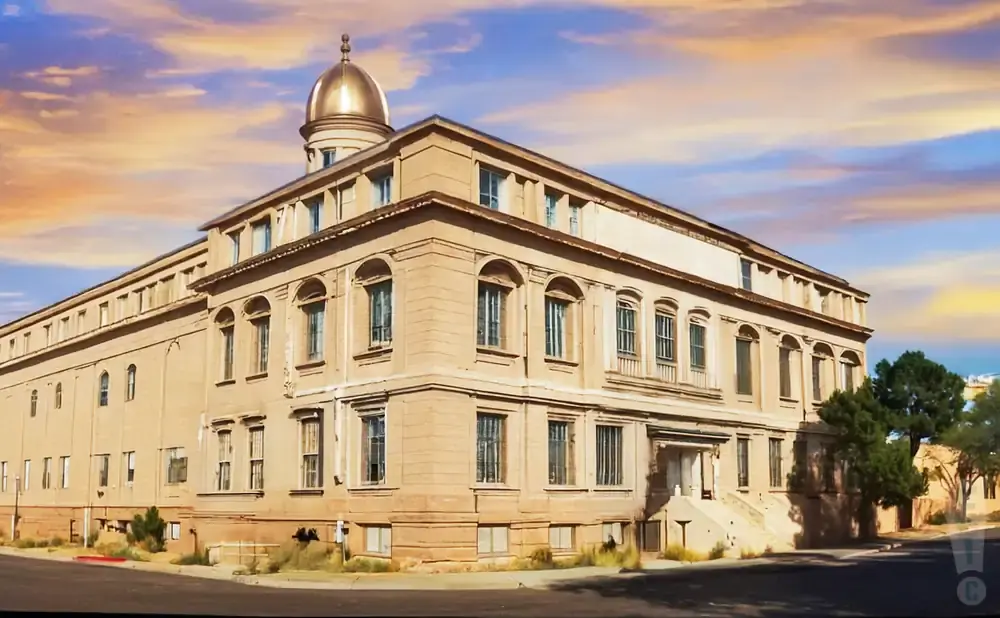 A tan, three-story building with arched windows and a golden dome under a dramatic sky.