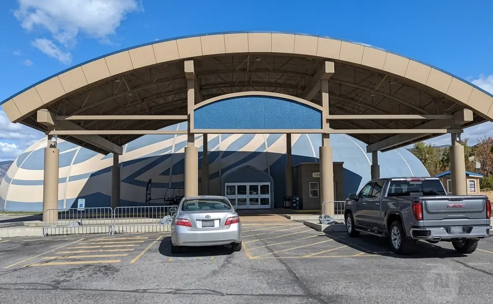 Silver sedan and grey GMC truck parked in front of a domed building with a wide, beige overhang.